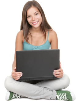 A young woman is sitting on the ground holding a laptop computer, looking at the camera and smiling.