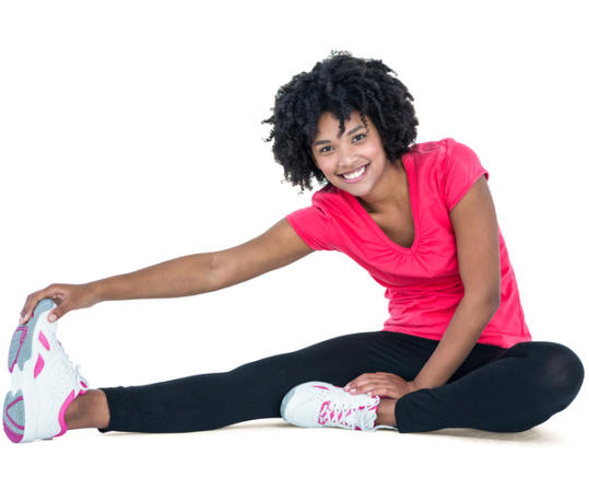 A young woman in athletic wear is sitting on the floor stretching her right leg and touching her toes.