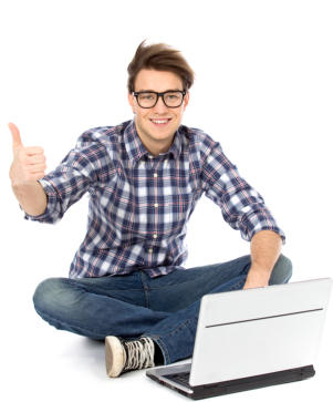 A man in his early twenties is sitting cross-legged on the floor with an open laptop on the floor in front of him. He is looking at the camera and smiling, doing a thumbs-up sign.