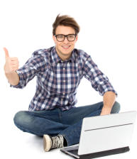 A man in his early twenties is sitting cross-legged on the floor with an open laptop on the floor in front of him. He is looking at the camera and smiling, doing a thumbs-up sign.