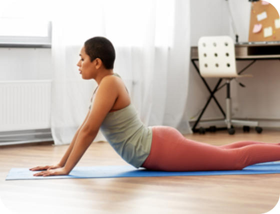 A woman is on her stomach on the floor in athletic wear. She is pushing up on her hands so her hips are pressed to the floor, her back is arched and her legs are straight