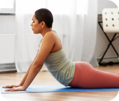 A woman is on her stomach on the floor in athletic wear. She is pushing up on her hands so her hips are pressed to the floor, her back is arched and her legs are straight