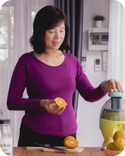 A senior woman stands in her kitchen making juice from oranges