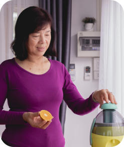 A senior woman stands in her kitchen making juice from oranges