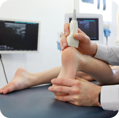 A medical technician uses an ultrasound wand to examine the heel of a young patient. The ultrasound screen image is in the background.