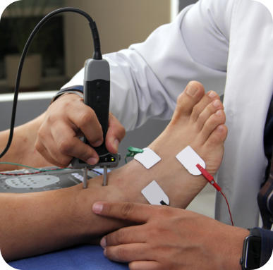 A medical professional is conducting a nerve study on a patient's foot. There are electrodes attached to the patient's foot and the technician is holding a wand on their ankle. 