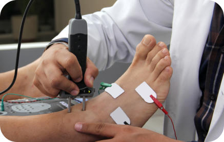 A medical professional is conducting a nerve study on a patient's foot. There are electrodes attached to the patient's foot and the technician is holding a wand on their ankle. 