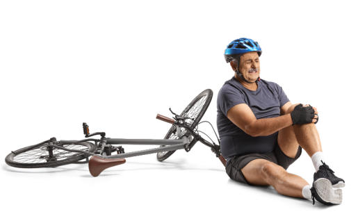 A senior man in athletic clothing and a bicycle helmet sits on the ground holding his knee and grimacing. His bike is lying on the ground next to him.