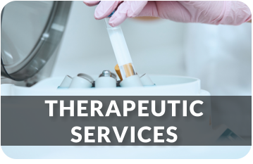 A medical technician wearing gloves removes a tube from a centrifuge machine. The image links to the Therapeutic Services page.