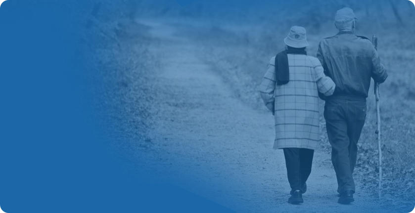 An elderly couple is dressed in warm clothing and walking arm in arm down a path. The man is holding a walking stick. The image is a background for the patient review displayed on the page.